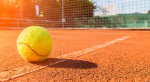 Das Bild zeigt einen Tennisball der auf einem Aschenplatz liegt im Hintersieht msn das Netz