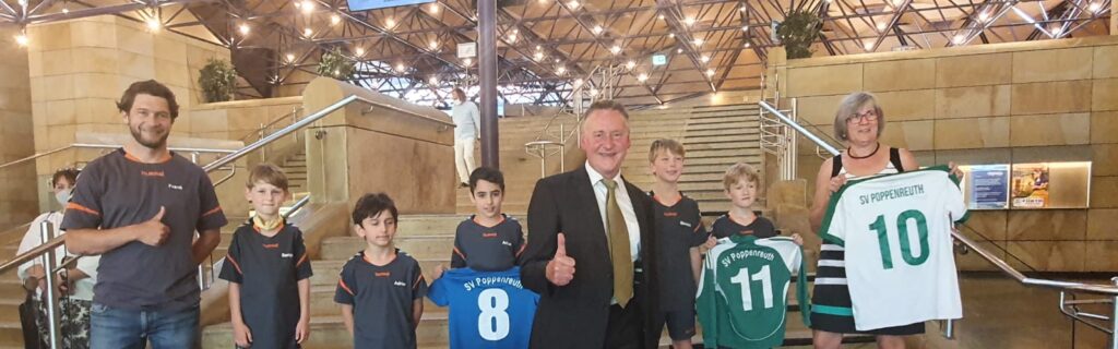 Das Bild zeigt mehrere Erwachsene und Kinder die T-Shirts vom SV Poppenreuth hochhalten