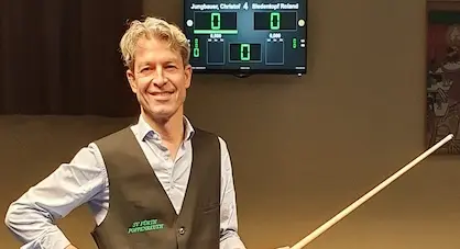 Das Bild zeigt einen Mann in einer Billardhalle der einen Queue in der Hand hält.